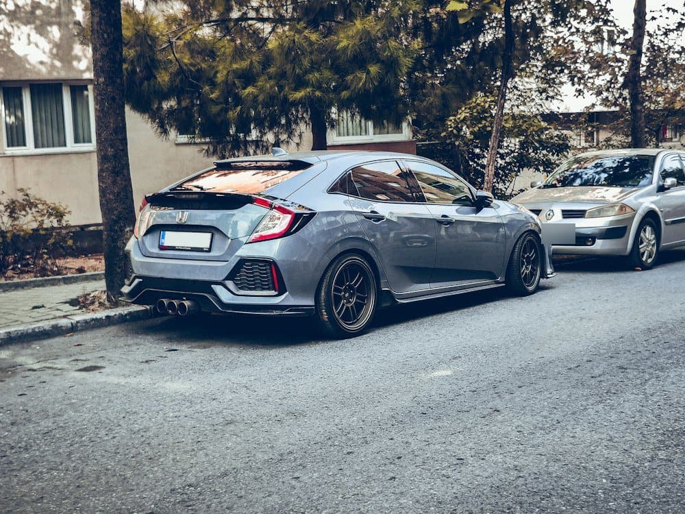 Ağaçlı bir sokakta park etmiş gri hatchback, arkadan çapraz